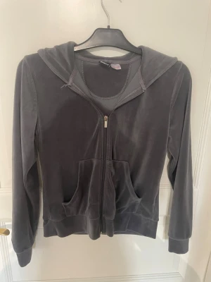 Grå velourhoodie från Gina Tricot - Mjuk och skön grå zip-hoodie i velour från Gina Tricot. Tröjan har dragkedja framtill, två stora fickor och en huva. Perfekt för en avslappnad och trendig look. Klassisk passform och ribbade muddar vid ärmslut och nederkant.