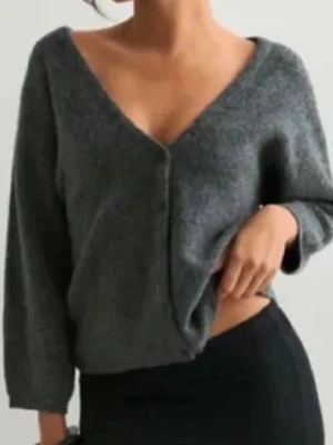 Grå kofta med v-ringning -  grå kofta med djup v-ringning och knäppning framtill. Koftan har trekvartsärmar, perfekt att slänga på sig över ett linne eller t-shirt. Tillverkad i ett mjukt, stickat material.