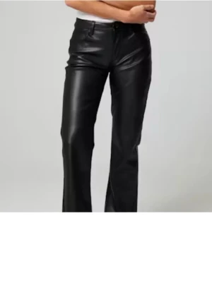 Svarta byxor  i skinnimitation - Snygga svarta byxor med rak passform i skinnimitation. Byxorna  har låg medel hög midja klassiska fickor och stängs med knapp och dragkedja. Perfekta för en trendig och edgy look.