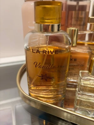 Vanilla parfym - La Rive Vanilla Touch är en parfym med söt vaniljdoft. Flaskan är rundad och genomskinlig med guldfärgat lock och detaljer. Innehållet har en varm, gyllene ton som matchar den mjuka och krämiga doften av vanilj. Perfekt för dig som älskar söta och mysiga dofter.