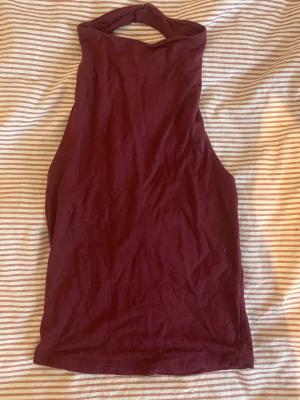 Mörkröd ärmlös halternecktop - Mörkröd ärmlös halternecktop i mjuk bomull. Toppen har hög hals och öppen rygg, vilket ger en trendig och stilren look. Perfekt att matcha med jeans eller kjol för en snygg outfit.