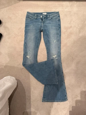 Blå bootcut jeans med broderade fickor - Säljer ett par ljusblå bootcut jeans med slitningar framtill och snygga broderade detaljer på bakfickorna. Jeansen har låg midja och klassisk femficksmodell. Perfekta för dig som gillar en avslappnad men trendig stil. Jag drog av prislappen innan jag testade dom så dom är helt nya och aldrig använda!💕