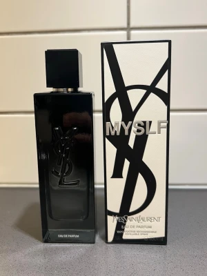 Yves Saint Laurent MYSLF Eau de Parfum - Säljer en elegant parfym från Yves Saint Laurent, MYSLF Eau de Parfum. Flaskan är svart med en stor YSL-logga i relief och har en stilren, fyrkantig form. Förpackningen är vit och svart med grafisk design och tydlig logotyp. Perfekt för dig som gillar exklusiva dofter.