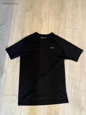  Under Armour S - Svart sportig t-shirt från Under Armour med korta ärmar och rund hals. Tillverkad i ett lätt och snabbtorkande funktionsmaterial som passar perfekt till träning. Diskret logga på bröstet.