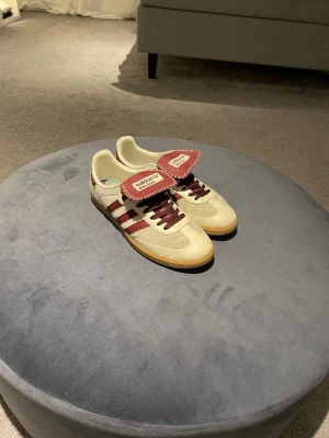 Adidas Wales Bonner sneakers beige/vinröd - Unika Adidas Wales Bonner sneakers i beige mocka med vinröda detaljer och snörning. Skorna har en klassisk låg siluett, gummisula och tydliga Wales Bonner-detaljer på plösen. Perfekta för dig som gillar retrostil och snygga färgkombinationer.
