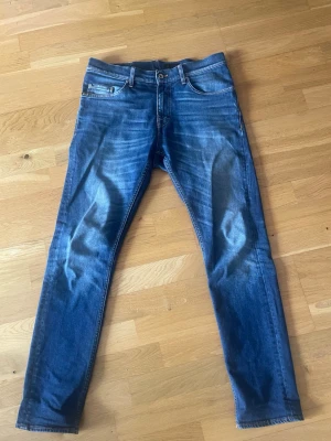 Blå slim fit jeans med slitningar - Snygga blåa tiger of sweden jeans i slim fit med lätt slitna detaljer och klassisk femficksdesign. Jeansen har normal midja och smal passform hela vägen ner. Perfekta för en trendig och avslappnad look.