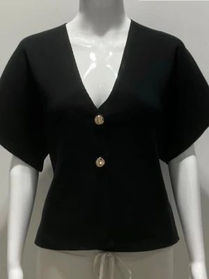 Svart topp med knappar - Stilren svart topp med v-ringning och två dekorativa guldknappar framtill. Modellen har korta, vida ärmar och en rak passform. Perfekt att styla med både jeans och kjol för en trendig look. I lappen står det storlek M/L men den passar mig som vanligt vis har storlek S eller M. Har aldrig använt. Köpt på Missäy i Göteborg. Ny pris 400. Pris kan diskuteras.