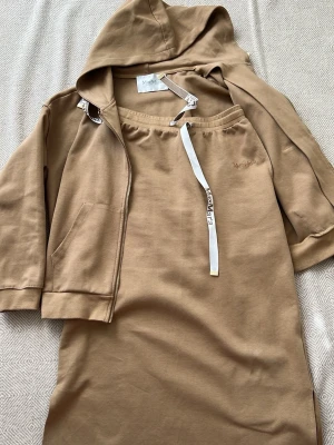 Max Mara Beige loungewear-set  - Mysigt loungewear-set från MaxMara i beige bomull. Setet består av en hoodie med dragkedja, fickor och vita snören med logga samt en matchande t-shirtklänning med samma snördetalj. Perfekt för chill dagar hemma. Storlek XL passar även S M L Köpt i Japan för 4500kr på vintage.
