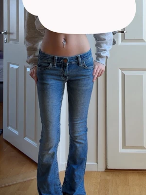 Blå bootcut jeans med kontrastsömmar - Säljer ett par blå bootcut jeans med låg midja och snygga kontrastsömmar på bakfickorna. Storleken är 152 men passar mig som är ca 160 Jeansen har klassisk femficksdesign och kopparfärgade knappar. Perfekta för dig som gillar en avslappnad men trendig look. 