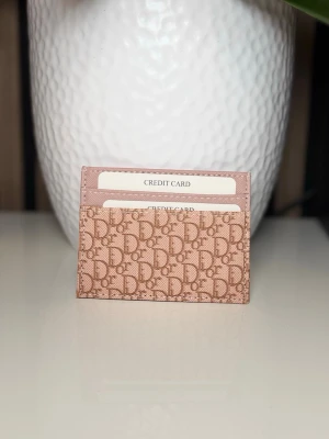 Rosa  korthållare med monogram - . Har flera fack för kort och är tillverkad i canvas med läderdetaljer. Perfekt för dig som vill ha en stilren och lyxig accessoar i väskan.