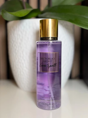 Victoria's Secret Love Spell mist - Fräsch och söt body mist från Victoria's Secret i doften Love Spell. Flaskan är genomskinlig med lila vätska och har ett elegant guldigt lock. Rymmer 250 ml och är perfekt att spraya på för en fruktig och blommig doft.