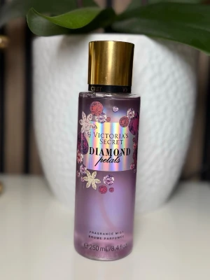 Victoria's Secret Diamond Petals mist - En snygg parfymmist från Victoria's Secret i doften Diamond Petals. Flaskan är lila med blommiga och glittriga detaljer samt ett guldigt lock. Rymmer 250 ml och har en feminin och fräsch design som sticker ut på hyllan.