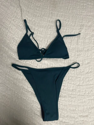 Mörkblå ribbad bikini med knyt - Snygg mörkblå bikini med ribbad struktur och knyt i toppen. Klassisk trekantsmodell med smala axelband och matchande bikinitrosa med högt skuren passform. Perfekt för strandhäng och poolparty.