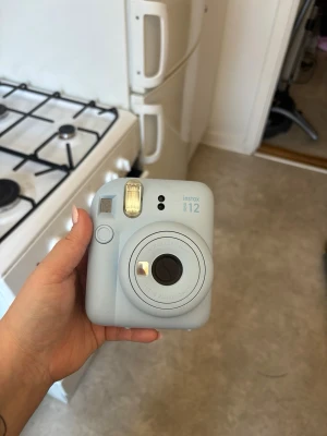 Fujifilm Instax Mini 12 blå kamera - Säljer en ljusblå Fujifilm Instax Mini 12 direktfilmskamera. Själva skalet till batteridelen har försvunnit :( annars funkar perfekt. Du får med ca 10 film till den!