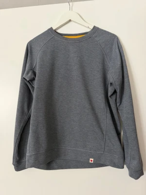 Grå High Coast Lite sweater från Fjällräven - Säljer en grå High Coast Lite sweater från Fjällräven med regular fit. Tröjan har rund hals, långa ärmar och diskret logotyp vid nederkanten. Materialet är lätt och bekvämt, perfekt för dig som gillar stilren design.