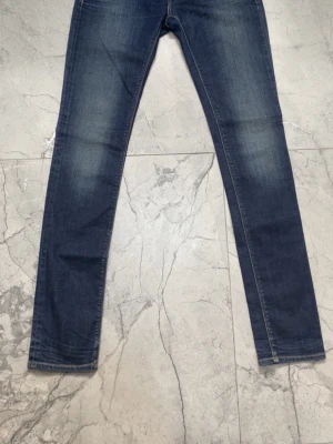 Blå slim fit jeans - Säljer ett par blå slim fit jeans med klassisk femficksdesign och snygga slitningar på framsidan. Jeansen har raka ben och är tillverkade i denim med stretch för extra komfort. Perfekt för dig som gillar en modern och stilren look.
