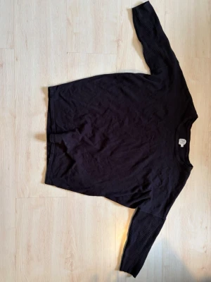 Svart långärmad tröja - En enkel svart långärmad tröja med rund hals. Tröjan har en rak passform och är tillverkad i ett mjukt material som passar perfekt till olika outfits. Stilren och lätt att matcha.