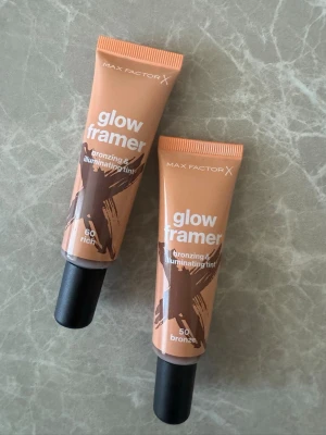 Max Factor Glow Framer  - Två tuber Max Factor Glow Framer bronzing & illuminating tint i nyanserna 60 rich och 50 bronze. Tuben är beige med svart kork och rymmer 30 ml. Perfekt för att ge huden en solkysst och glowig finish.