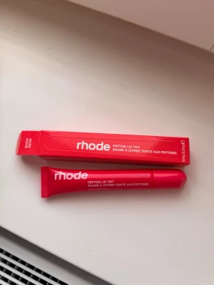Rhode Peptide Lip Tint Läppbalsam guavaspritz - Rhode Peptide Lip Tint läppbalsam (guava spritz). Självklart helt oanvänd, fick med i goodiebag men inget jag kommer ha användning av 🎈