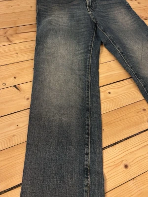 Blå straight fit jeans  - Säljer ett par blå straight fit jeans från H&M ALDRIG ANVÄNDA med klassisk femficksdesign och snyggt slitna detaljer. Jeansen har en rak passform och är tillverkade i denim med ljus tvätt. Perfekta för dig som gillar en avslappnad stil.