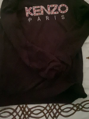 Svart hoodie från Kenzo Paris - Cool svart hoodie från Kenzo med broderad logga på bröstet och texten 'Kenzo Paris' i vitt och mönstrat. Mjuk bomullskänsla och klassisk passform med långa ärmar. Perfekt för dig som gillar streetstyle och exklusiva märken.