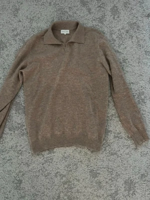 Beige kashmir tröja från Davida - Stickad tröja från Davida i mjuk beige ton. Tröjan har klassisk krage, långa ärmar och ribbade muddar vid ärmslut och nederkant. Perfekt för lager på lager och enkel att matcha med olika outfits. Den är även gjord av 100 Kashmir. Storlek S men sitter snarare som M.