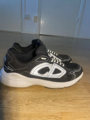 B30 skor - Säljer ett par svarta sneakers från CD med vit sula och vita detaljer. Skorna har en chunky design, mesh och syntetmaterial, samt vita snören. CD-loggan syns tydligt på sidan och bak. Perfekt för dig som gillar sportig och modern stil.