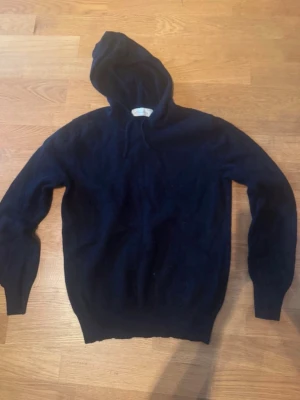 Mörkblå hoodie i mjukt material - Säljer en enkel och stilren mörkblå hoodie med huva och ribbade muddar. Hoodien är tillverkad i ett mjukt och skönt material, perfekt för att chilla eller hänga med kompisar. Klassisk passform och dragsko i huvan.