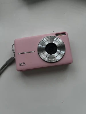Rosa digitalkamera 44MP 16x zoom - Säljer en rosa digitalkamera med 44 megapixlar och 16x powerful zoom. Kameran har en stor display på baksidan, flera funktionsknappar och handledsrem. Objektivet är i silverfärgad metall och kameran har en kompakt, rektangulär form. Perfekt för dig som vill ta snygga bilder. Laddare medföljer. Priset kan diskuteras.