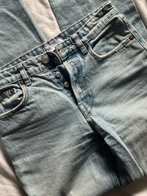 Ljusblå raka jeans från Zara - Säljer ett par ljusblå jeans från Zara med raka ben och hög midja. Jeansen har klassisk femficksdesign, synliga knappar i gylfen och är gjorda i denim. Perfekta för en avslappnad och trendig look.