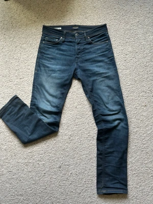Mörkblå slim fit jeans från Jack & Jones - Snygga mörkblå slim fit jeans från Jack & Jones med klassisk femficksdesign och lätt slitna detaljer framtill. Jeansen har normal midja, raka ben och är tillverkade i stretchigt denim för extra komfort.