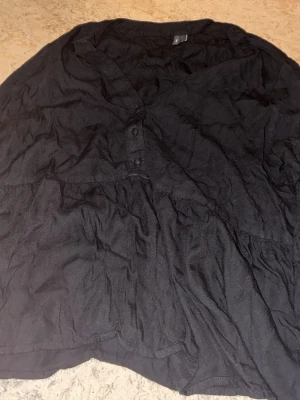 Svart omlottklänning med knappar - Svart klänning med omlott-design och knappar framtill. Klänningen har en luftig form och är tillverkad i ett lätt bomullsmaterial. Perfekt för dig som gillar en enkel och stilren look.