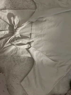 Vit omlottopp med knyt - Trendig vit omlottopp med knyt baktilll och korta ärmar. Toppen har en clean look och är tillverkad i mjukt bomullstyg som känns skönt mot huden. Perfekt för dig som gillar minimalistisk stil och vill ha något enkelt men ändå snyggt.