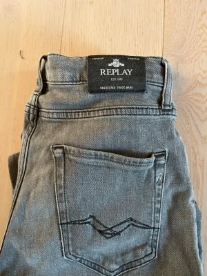 Grå jeans från Replay - Säljer ett par grå jeans från Replay, THAD-modellen med klassisk femficksdesign och snygga detaljer på bakfickan. Jeansen har en normal passform med raka ben. Replay storleken finns på sista bilden.
