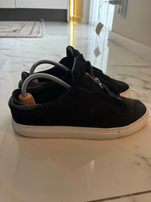 Axel Arigato laceless med dragkedja  - Säljer ett par svarta sneakers i mocka med vit sula och dragkedja. Storlek 41 utan box