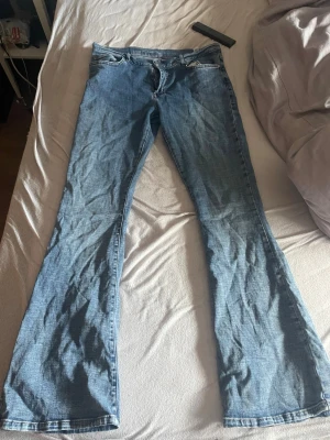 Blå low flare jeans med längd 32 - Säljer ett par blå low flare jeans med längd 32 och midja M. Klassisk femficksdesign och snyggt utsvängda ben. Perfekt för dig som gillar retrostil och vill ha ett par jeans som sticker ut. Materialet är denim och färgen är ljusblå.