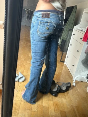 Lågmidjade bootcut jeans - Säljer ett par blå bootcut jeans med snygga detaljerade fickor bak och fram. Jeansen har en låg midja. Märket är Lee, midjemått är 38cm och jag är 158cm lång, de är lite långa på mig 