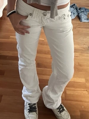 Vita jeans med låg midja - Säljer ett par vita jeans med låg midja och bootcut ben. Jeansen har klassiska fem fickor och silverfärgade knappar. Perfekta för dig som gillar en clean och fräsch look. Materialet är denim och de är riktigt bekväma. 