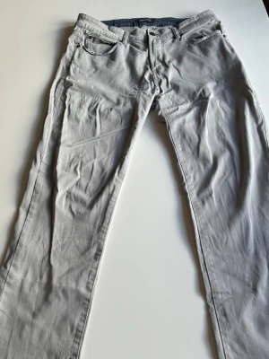 Ljusgrå chinos från Dressmann - Snygga ljusgrå chinos från Dressmann i regular fit. Klassisk femficksmodell med knappgylf och bälteshällor. Tillverkade i mjukt bomullstyg som ger en skön känsla och stilren look. Perfekta för dig som vill ha ett par stilrena och bekväma byxor.