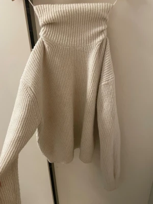 Beige polotröja i ribbstickat - Säljer en beige ribbstickad polotröja med hög krage och långa ärmar. Tröjan har en oversized passform och är gjord i mjukt, tjockt material som känns riktigt cozy. Perfekt för kyliga dagar och enkel att styla till olika outfits.