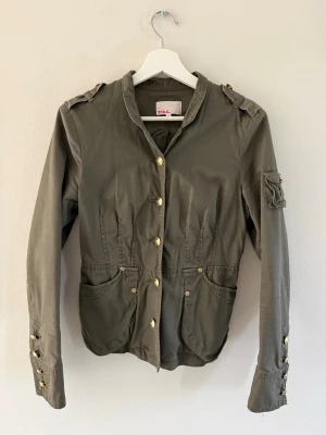 Olivgrön jacka från Zoul med guldknappar - Stilren olivgrön jacka från Zoul med guldknappar, axelklaffar och fickor fram. Storlek 38 vilket motsvarar xs-m i passform och är i bra skick.
