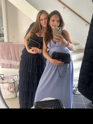 Bal klänning - Säljer en marinblå långklänning med flera lager volanger och smickrande v-ringning. Klänningen har smala axelband och är tillverkad i ett lätt, transparent tyg som ger en elegant känsla. Perfekt för speciella tillfällen.