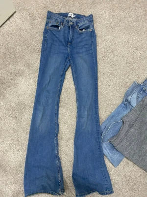 Blå bootcut jeans från lager  storleken Xs - Säljer ett par klassiska blå bootcut jeans från lager med hög midja och fem fickor. Jeansen har en snygg tvätt och utsvängda ben som ger en retrovibe. Perfekta för dig som gillar en avslappnad men trendig stil.