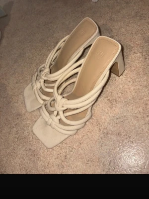 Beige sandaler med klack från H&M - Säljer ett par trendiga beige sandaler från H&M i storlek 41. De har fyrkantig tå, tjock klack och flera flätade remmar i tygmaterial som ger en cool och modern look. Perfekta för dig som vill sticka ut med snygga detaljer och bekväm passform.