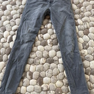 Gråa slim fit jeans från Replay - Säljer ett par gråa slim fit jeans från Replay med klassisk femficksdesign och svarta detaljer. Jeansen har normal midja och dragkedja med knapp. Snygg tvätt och diskreta sömmar gör dem perfekta till en avslappnad stil.