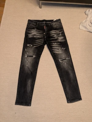 Dsquared2 jeans - Säljer ett par svarta skinny jeans med slitningar och distressed detaljer framtill och baktill. Jeansen har en tvättad look med ljusare partier och klassisk femficksmodell. Perfekta för en edgy streetstyle. Materialet är denim.