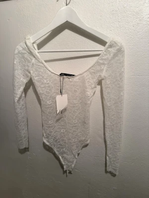 Vit spetsbody från Zara - Säljer en snygg vit body från Zara i genombruten spets med lång ärm och djup ringning.❤️❤️nypris 299kr med prislapp kvar