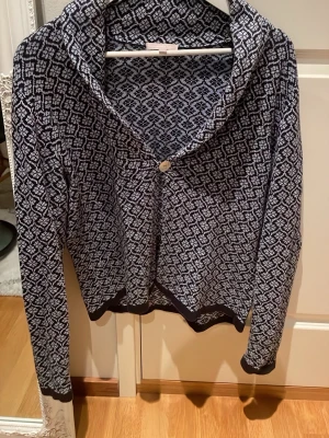 Mönstrad kofta med sjalkrage i strl M från Sincerely Loved - Snygg mariblå och vit mönstrad kofta med grafiskt mönster och sjalkrage. Koftan har en knapp framtill och ribbade muddar vid ärmslut och nederkant. Perfekt för lager på lager och ger en stilren look till din outfit.