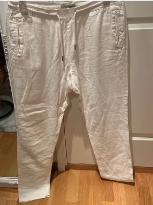 Vita linnebyxor från ¡Solid i strl L med fickor baktill - Säljer ett par vita linnebyxor från Solid med dragsko i midjan och fickor på sidorna och baktill. Byxorna har en avslappnad passform och är tillverkade i ett mjukt material som känns skönt mot huden. Perfekta för chill dagar eller när du vill ha det bekvämt.