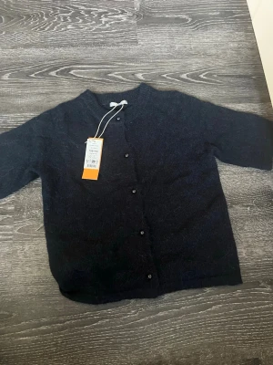 Mörkblå kofta från Gina  - Mysig mörkblå kofta från Gina med rund halsringning och knappar framtill. Koftan har halvlånga ärmar och är tillverkad i ett mjukt, stickat material som ger en avslappnad look. Perfekt att slänga över en topp eller klänning.